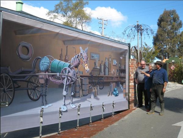 Tonnie Spijkerbosch (R) explaining finer details of new Steptoe's yard screen artwork to Alastair and Noelene Swan (flowers in background made from old hay rack and plumbing fittings).